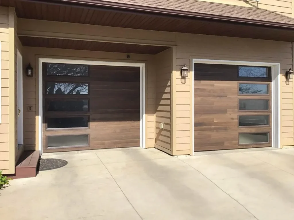 Two modern, dark-wood plank sectional garage doors featuring vertically stacked rectangular glass windows along one side, beautifully highlighting a contemporary garage door style.