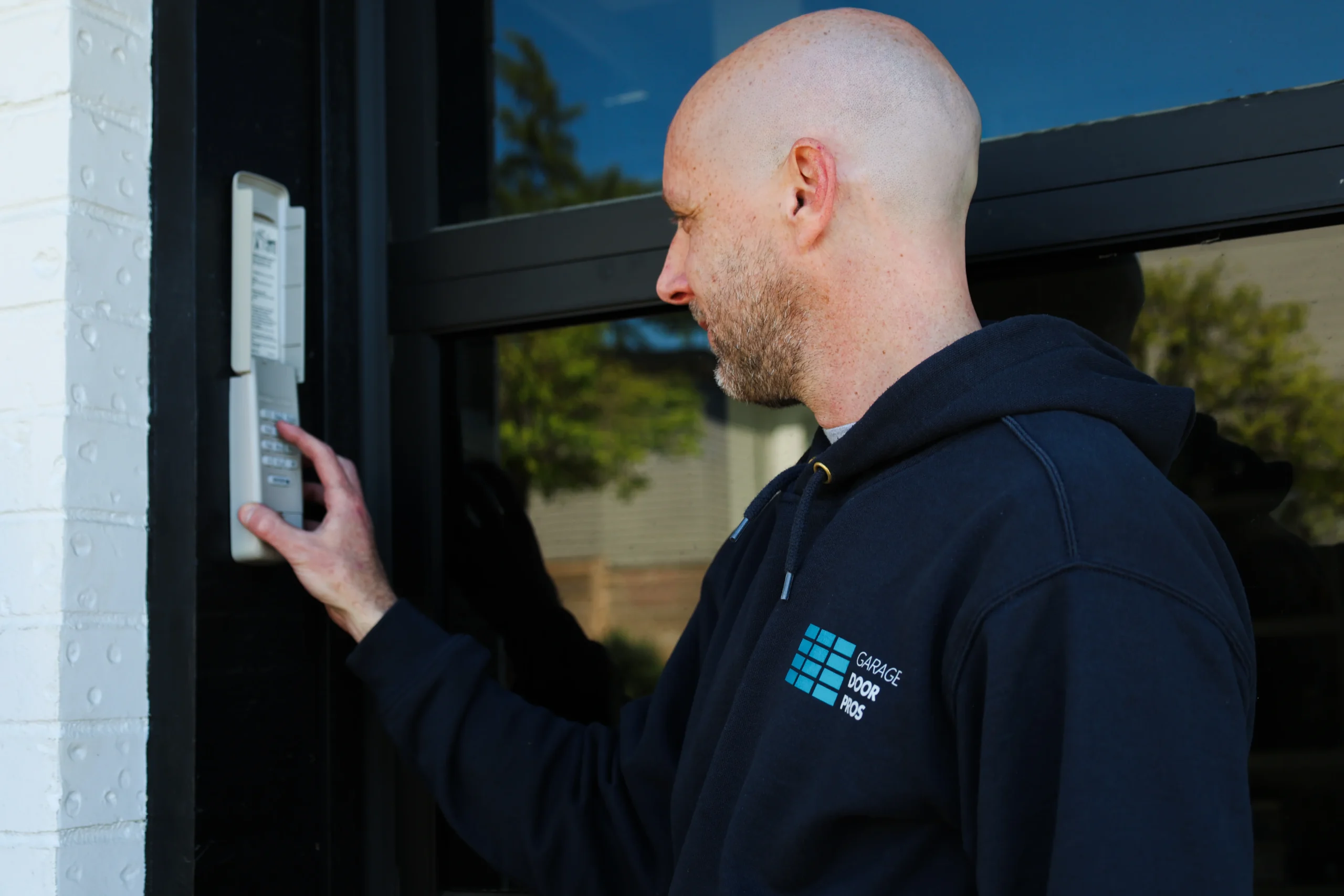 A professional technician programing or testing an outdoor wireless entry system mounted next to a glass-paneled door, demonstrating the convenience and security of electronic keypad locks.