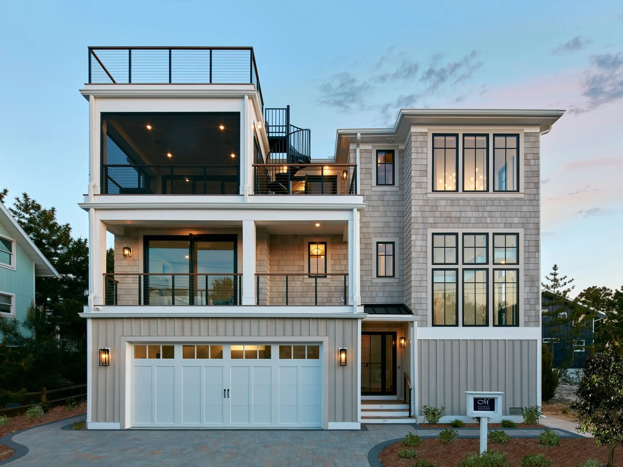 A crisp white carriage-house style garage door with top window panes seamlessly blends into the facade of a multi-story coastal modern residence, proving that garage door style matters for modern homes.