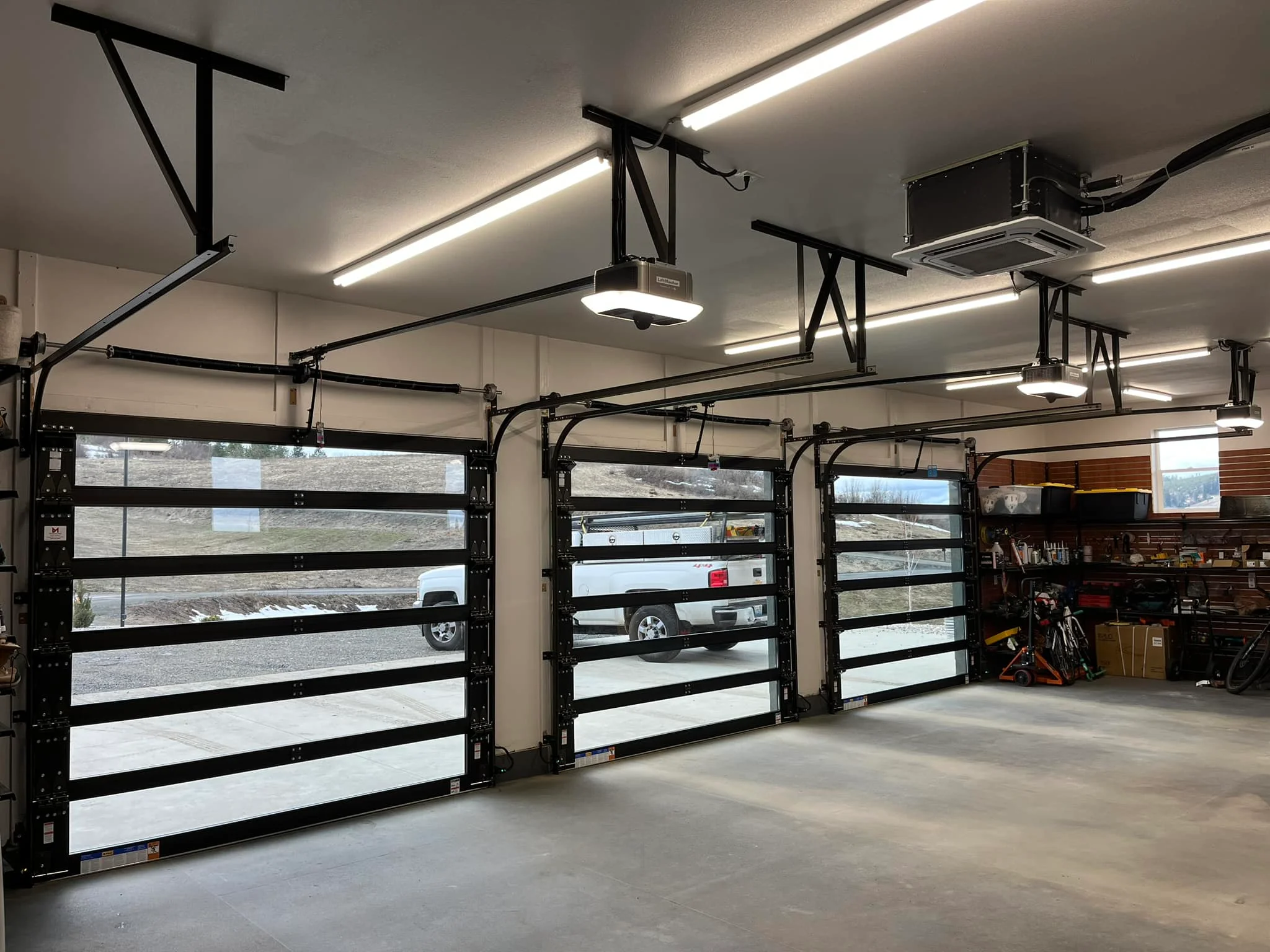 An interior view of a well-lit, spacious garage featuring three modern glass-paneled sectional doors with black frames, each equipped with overhead automatic openers that support advanced garage door security upgrades.